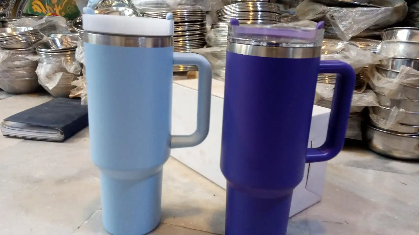 Two insulated travel mugs, one blue and one purple, on a wooden surface with metal containers in the background.