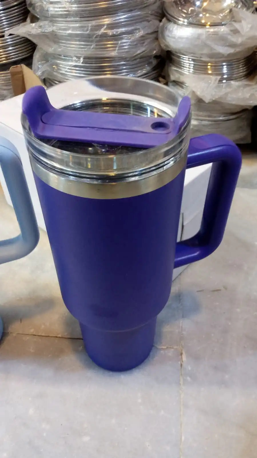 Blue mug with a purple handle and lid on a reflective surface.