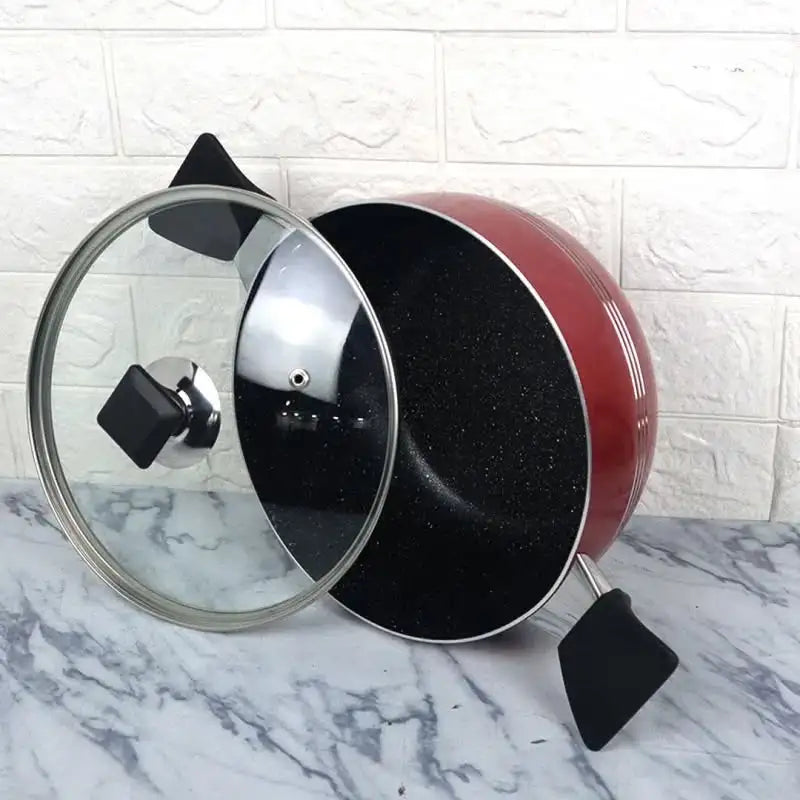 Red frying pan with a glass lid on a marble surface with a tiled wall background