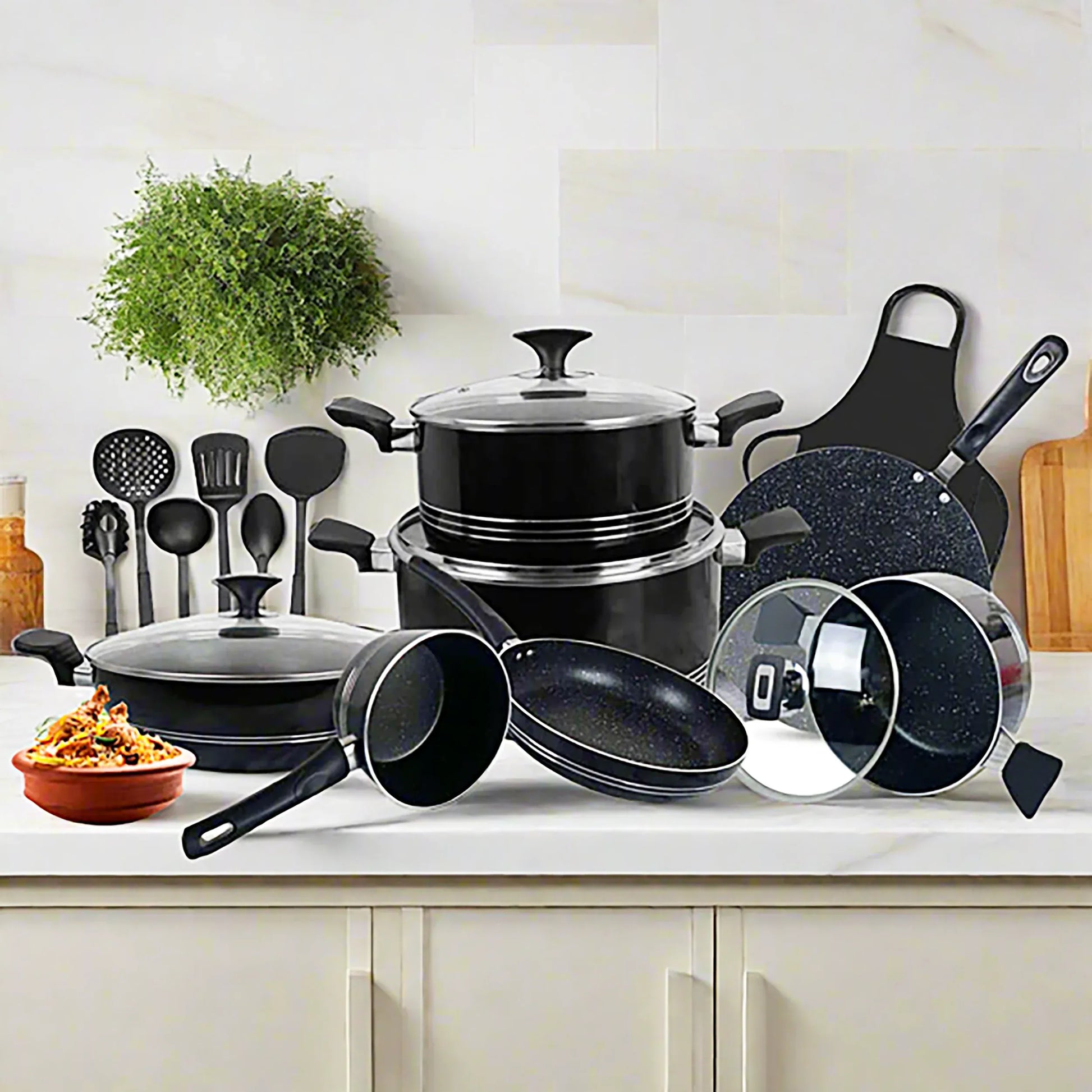 Set of black cookware on a kitchen counter with utensils and a plant in the background.