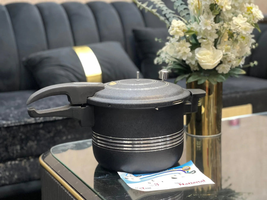 Black pressure cooker on a glass table with a vase of flowers in the background