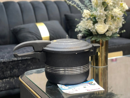 Black pressure cooker on a glass table with a vase of flowers in the background